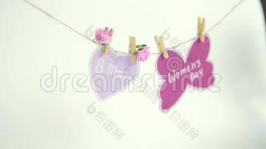<strong>妇女节</strong>`快乐.. <strong>妇女节</strong>`纸上，挂在一根绳子上，靠近一颗粉红色的心，上面装饰着鲜花，背景白色。